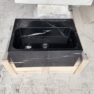 以下が含まれることがあります： 木製の箱の上に置かれた、白の筋が入った黒い大理石のシンク。シンクは長方形で、中央に排水口があります。