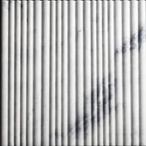 May include: A rectangular, white marble panel with vertical, ridged detailing. The ridges create a series of parallel lines across the surface. Subtle grey veining adds depth and visual interest to the stone. The background is solid black.
