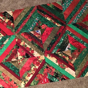 May include: A handmade Christmas quilt featuring a patchwork design. The quilt showcases a variety of fabrics in red, green, and gold, with patterns including poinsettias and stripes. The quilt's dimensions are approximately 60 inches by 70 inches.