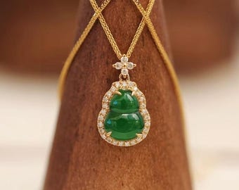 May include: A gold necklace with a pendant featuring a green jade Buddha-shaped charm. The charm is surrounded by small, clear gemstones. The necklace is displayed on a brown stand.
