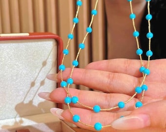 May include: A gold chain necklace with turquoise blue beads. The necklace is displayed on a hand and in a red box.