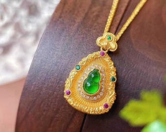 May include: A gold pendant necklace with a green jade gourd charm. The pendant is set with small diamonds and green and red gemstones. The necklace is on a wooden surface.