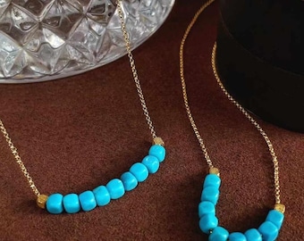 May include: Two gold necklaces with turquoise beads. The shorter necklace has a curved shape, while the longer necklace is straight.
