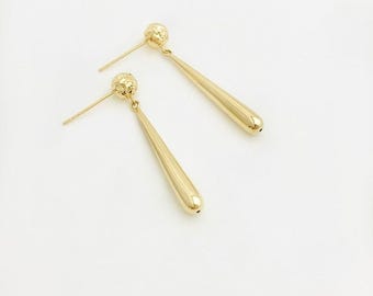 Pode incluir: Um par de brincos pendurados dourados. Cada brinco apresenta um pino de bola texturizado e um pingente longo em forma de gota. Os brincos são exibidos em um fundo branco.