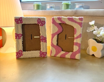 May include: Two white picture frames with pink accents. One frame has a pink bow design and the other has a pink wavy design.