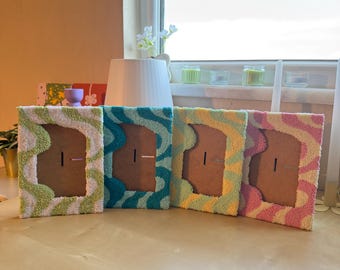 May include: Four colorful, textured picture frames with wavy patterns. The frames are in shades of green, teal, yellow, and pink. Each frame has a brown backing with a slot for a photo. The frames are displayed on a light-colored wooden surface.