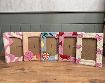 May include: Five colorful picture frames with different designs. The frames are made of a soft, textured material and feature various summer-themed patterns, including seashells, fruit, and bows.