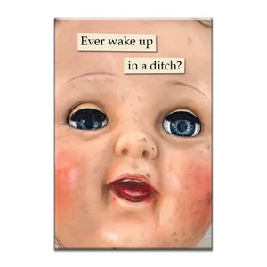 Puede incluir: Una cabeza de muñeca vintage con ojos azules y una boca abierta de par en par. La cara de la muñeca está sucia y desgastada. El texto "Ever wake up in a ditch?" está escrito sobre un fondo beige encima de la cabeza de la muñeca.