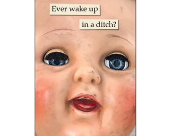 May include: A vintage doll's head with blue eyes and a wide open mouth. The doll's face is dirty and worn. The text "Ever wake up in a ditch?" is written on a beige background above the doll's head.