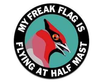 May include: A black and white circular sticker with the text "My Freak Flag Is Flying At Half Mast" around the edge. Inside the circle is a teal blue background with a red and grey bird with a red eye.