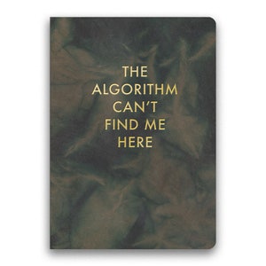 Op de afbeelding: Een donkergroen lederen notitieboek met de tekst "THE ALGORITHM CAN'T FIND ME HERE" in gouden letters.