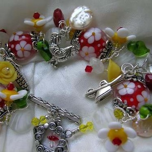 May include: A silver charm bracelet featuring red, white and yellow glass beads, silver charms and a small silver locket. The bracelet includes a variety of floral and garden-themed charms, such as a flower, a spade and a rooster.