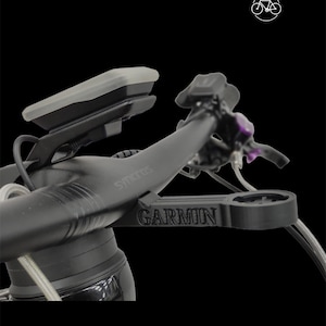 Puede incluir: Manillar de bicicleta negro con un soporte Garmin y un ordenador de ciclismo negro y gris. El manillar está etiquetado como "SYNTACE" y el soporte como "GARMIN".