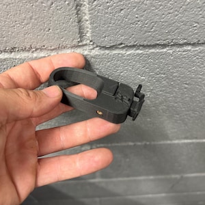 Könnte beinhalten: Ein schwarzer 3D-gedruckter Fahrradlicht-Halter mit einer kleinen Schraube. Der Halter hat eine Schlaufe zum Anbringen eines Lichts.
