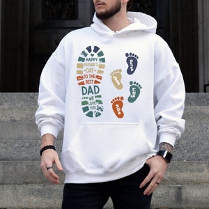 May include: White hoodie with a graphic design for Father's Day. The design includes a footprint shape with the text "Happy Father's Day to the Best Dad, We Love You." and several colorful footprints with names.