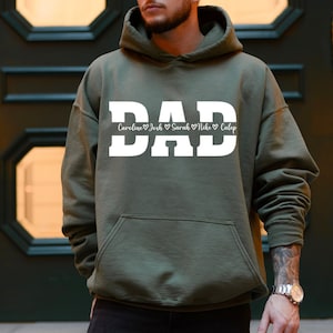 May include: Green hooded sweatshirt with the word "DAD" in white block letters. Below the word "DAD" is a line of text that reads "Caroline ♥ Josh ♥ Sarah ♥ Mike ♥ Caleb".