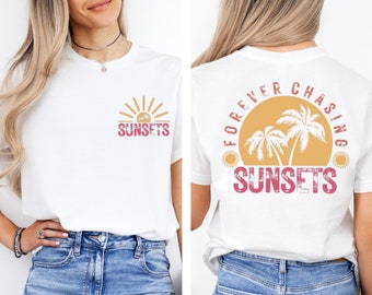 May include: White t-shirt with a sunset graphic on the front and back. The front features a sun and the word "SUNSETS" in pink and orange. The back has a sunset with palm trees and the words "FOREVER CHASING SUNSETS".