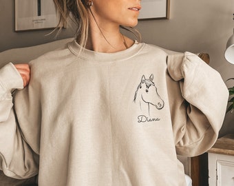 May include: A beige sweatshirt with a black outline of a horse's head and the name "Diana" printed on the front.