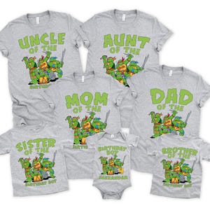 May include: A collection of gray t-shirts and a onesie featuring green text and graphics of Teenage Mutant Ninja Turtles. The shirts read "Uncle," "Aunt," "Mom," "Dad," "Sister," and "Brother" with "Birthday Boy" text. The onesie says "Birthday Boy Alexander."