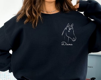 May include: Black sweatshirt featuring a white line drawing of a horse's head. The name "Diana" is written in cursive below the horse illustration. The sweatshirt is a solid black color.