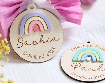 May include: Two wooden circle ornaments with rainbow designs and the names Sophia and Paul. Each ornament has a small heart and the text "Schulkind 2025". One ornament also has the text "Hipp, hipp, hurra!"