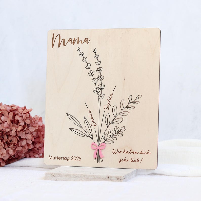 May include: Wooden sign with the word "Mama" at the top, a bouquet of flowers with the names "Sophia" and "Emelie" written on the stems, and the text "Muttertag 2025" and "Wir haben dich sehr lieb!" at the bottom.
