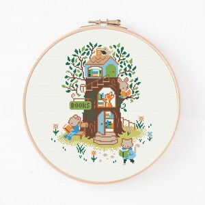 May include: Cross-stitch embroidery of a treehouse scene with woodland creatures. The treehouse has a green roof, brown trunk, and a sign that says "BOOKS". A mouse reads on a bench, a fox looks out a window, and a cat reads a book.