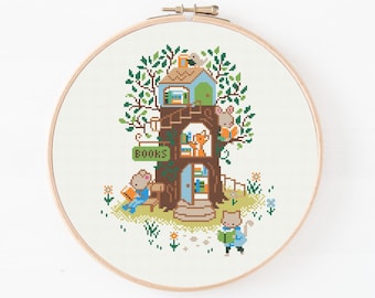 May include: A cross-stitch embroidery in a round wooden hoop featuring a brown tree house with multiple levels. The tree contains shelves of books, a sign that reads BOOKS, and several small animal characters reading books in and around it.
