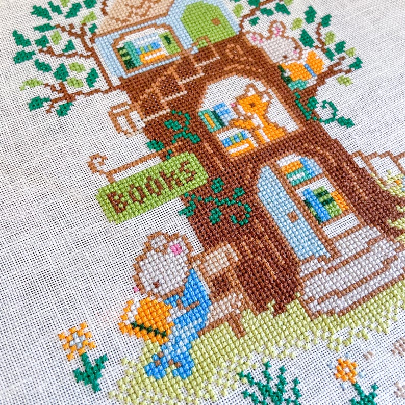May include: Cross-stitch of a treehouse with a sign that reads "BOOKS". The treehouse is brown with green, blue, and white accents. A bunny and fox are visible, along with books in the windows. The scene is set in a grassy area with flowers.