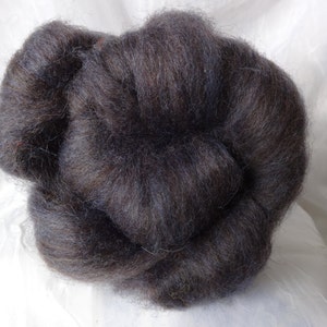 May include: A close-up of a dark brown and black wool roving. The roving is soft and fluffy, and it is perfect for spinning or felting.