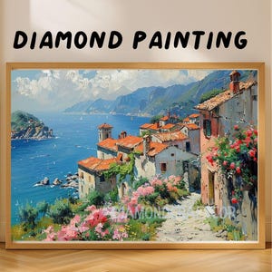 May include: A framed diamond painting featuring a coastal landscape with Mediterranean-style houses, red roofs, and pink flowers along a stone path overlooking a blue sea and mountains. The text DIAMOND PAINTING is printed above the artwork.