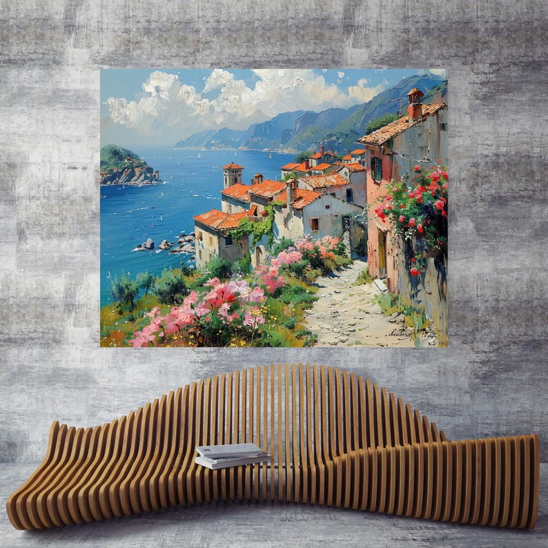May include: A rectangular wall art print depicting a coastal village with terracotta-roofed buildings, a stone path, and pink flowers overlooking a blue sea under a cloudy sky, mounted above a curved, slatted wooden bench on a gray wall.