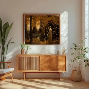 Puede incluir: Una impresi&oacute;n art&iacute;stica enmarcada representa a una mujer con un vestido dorado en un bosque con luces brillantes. La obra de arte utiliza tonos c&aacute;lidos de oro, marr&oacute;n y naranja, creando una atm&oacute;sfera serena y et&eacute;rea. La impresi&oacute;n se exhibe sobre un mueble de madera.