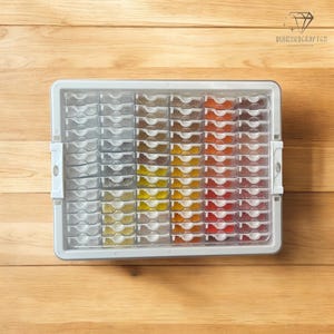 Op de afbeelding: Een transparante plastic opbergdoos met meerdere kleine vakjes gevuld met gekleurde kralen. De doos is gelabeld met "DiamondKraftGo".