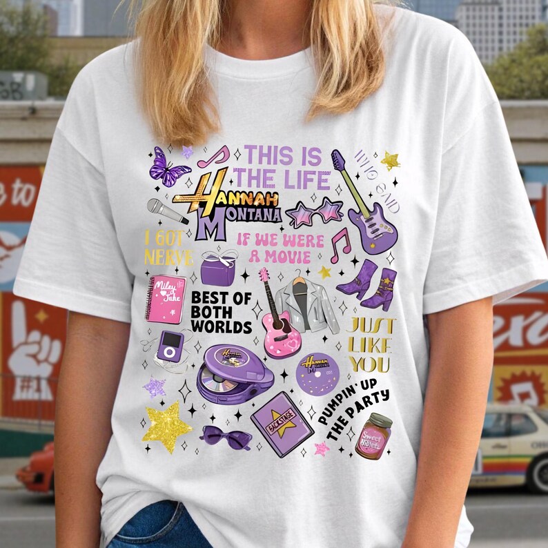 May include: White t-shirt featuring a colorful graphic design with the text "Hannah Montana" and various illustrations, including a guitar, stars, and the phrase "Best of Both Worlds."