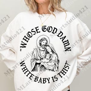 May include: White sweatshirt with a black graphic. The graphic features a religious image of a family with the text "WHOSE GOD DAMN WHITE BABY IS THIS?" in a circular design around the image.