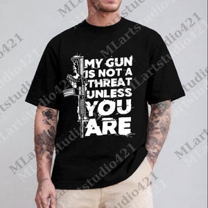 May include: Black t-shirt featuring a white graphic of a rifle and the text "MY GUN IS NOT A THREAT UNLESS YOU ARE". The design is centered on the front of the shirt.