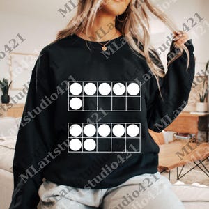 May include: Black sweatshirt featuring a white graphic of two ten-frames, each with ten circles. The sweatshirt is a solid black color. The graphic is a simple, clean design, perfect for math enthusiasts or educators.