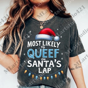 May include: Dark gray t-shirt with the text "MOST LIKELY TO QUEEF ON SANTA'S LAP" in white and blue. The design includes a Santa hat, snowflakes, and a string of Christmas lights. A humorous holiday tee.