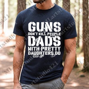 May include: Navy blue t-shirt with white text that reads "GUNS DON'T KILL PEOPLE DADS WITH PRETTY DAUGHTERS DO." The shirt also features small white bullet graphics. The shirt is short-sleeved.