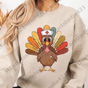Op de afbeelding: Een beige sweatshirt met een cartoon kalkoen met een verpleegsterspet en stethoscoop. De kalkoen heeft kleurrijke staartveren in tinten oranje, geel en rood. Het ontwerp is gecentreerd op de voorkant van het shirt.