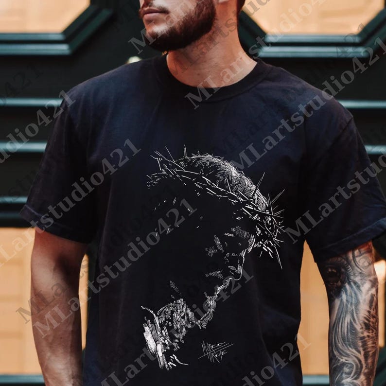 May include: Black t-shirt featuring a detailed white illustration of a person wearing a crown of thorns. The graphic is a side profile, with the face and crown in sharp focus against the dark fabric. The shirt is a classic crew neck.