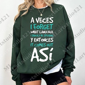 以下が含まれることがあります： 「A Veces I Forget What Language I Should Be Speaking Y Entonces It Comes Out Así」と書かれた白い文字が入った、濃い緑色のスウェットシャツ。スウェットシャツは長袖で、クルーネックです。