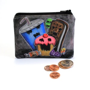 May include: A small, rectangular coin purse with a black zipper, featuring a colorful illustration of cartoon sweets. The design includes a blue soda, cupcake, ice cream sandwich, and candy. Several coins are scattered in front of the purse.