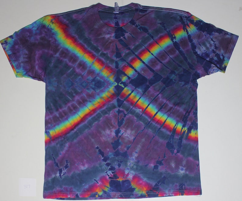 May include: A tie-dye t-shirt with a rainbow pattern on a dark blue background. The shirt has a relaxed fit and short sleeves.