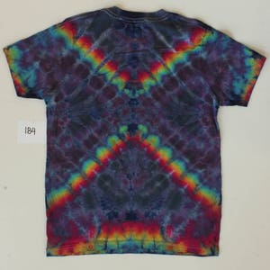 Może przedstawiać: Koszulka tie-dye z ciemnoniebieskim tłem i wzorem tęczy. Wz&oacute;r jest symetryczny i ma spiczasty kształt u dołu.