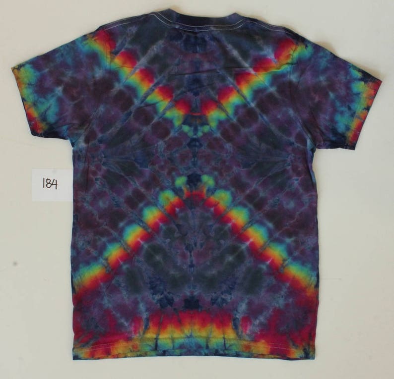 Może przedstawiać: Koszulka tie-dye z ciemnoniebieskim tłem i wzorem tęczy. Wz&oacute;r jest symetryczny i ma spiczasty kształt u dołu.
