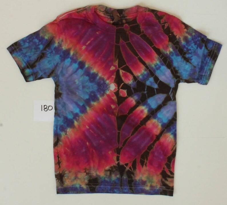 Puede incluir: Una camiseta tie-dye con fondo marr&oacute;n oscuro y un dise&ntilde;o colorido de azul, rojo y morado. La camiseta tiene cuello redondo y mangas cortas.