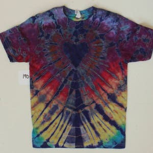 K&ouml;nnte beinhalten: Ein Batik-T-Shirt mit einem blauen Herzen in der Mitte. Das Shirt ist eine Mischung aus lila, rot, gelb und blauen Farben.