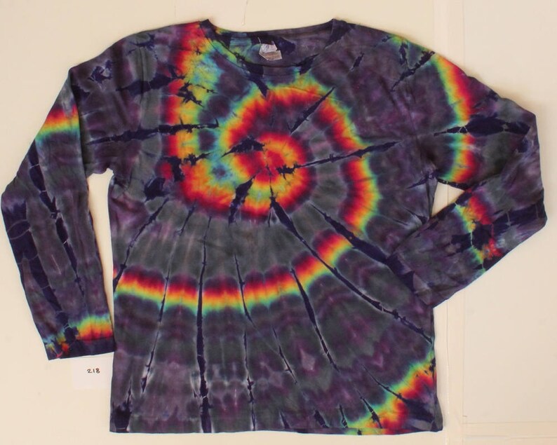 May include: A long-sleeved tie-dye shirt with a spiral design. The shirt has a dark base colour with bright rainbow shades of red, orange, yellow, green, and blue radiating from the centre. It has a crew neck and is made of a soft material.